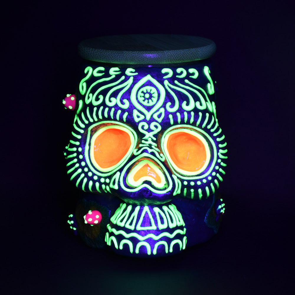 Pulsar Sugar Skull Glass Jar glowing in the dark, front view, perfect for storing rolling accessories