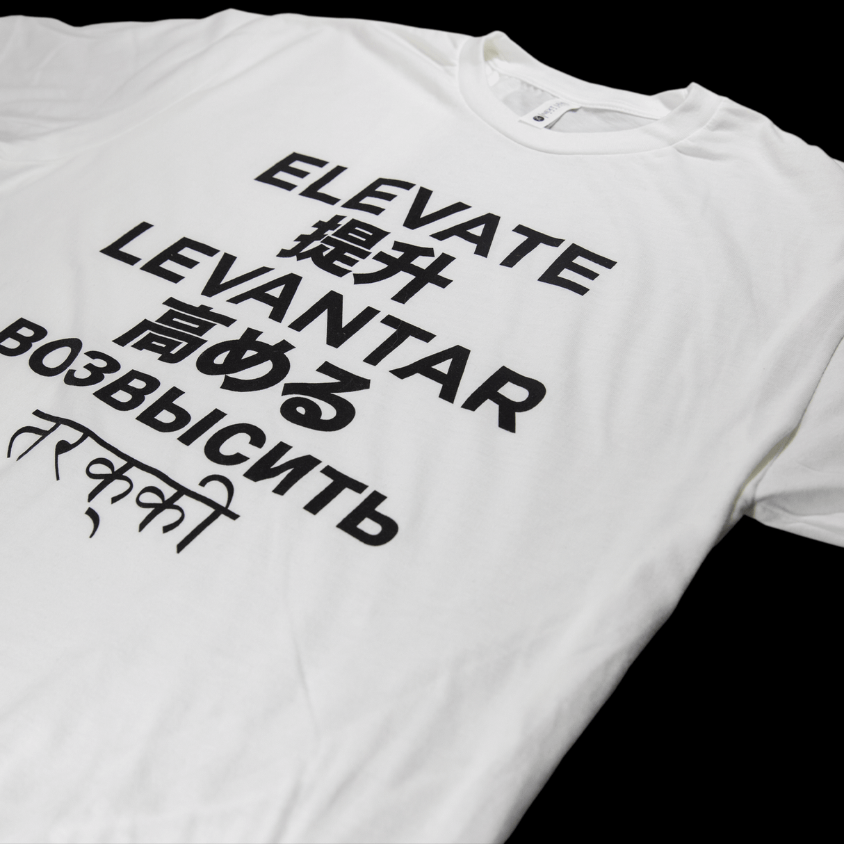 MJ Arsenal Elevate T-Shirt in white with multilingual black text design, top view on a dark background