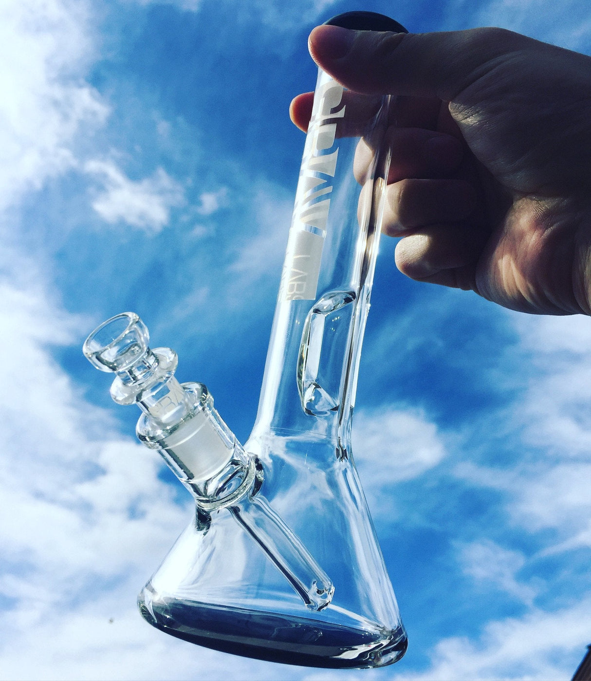 Hand holding GRAV Beaker Bong with Geometric Ice Pinch against a blue sky