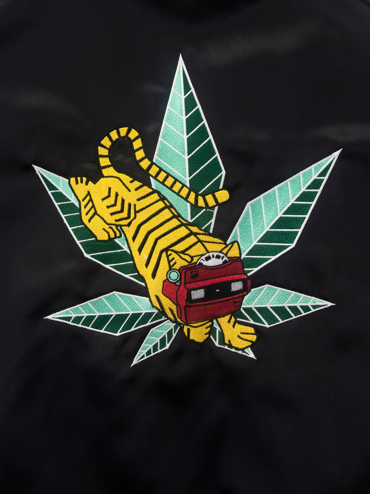 Close-up of GRAV Satin Bomber Jacket with iconic leaf and tiger design, black apparel