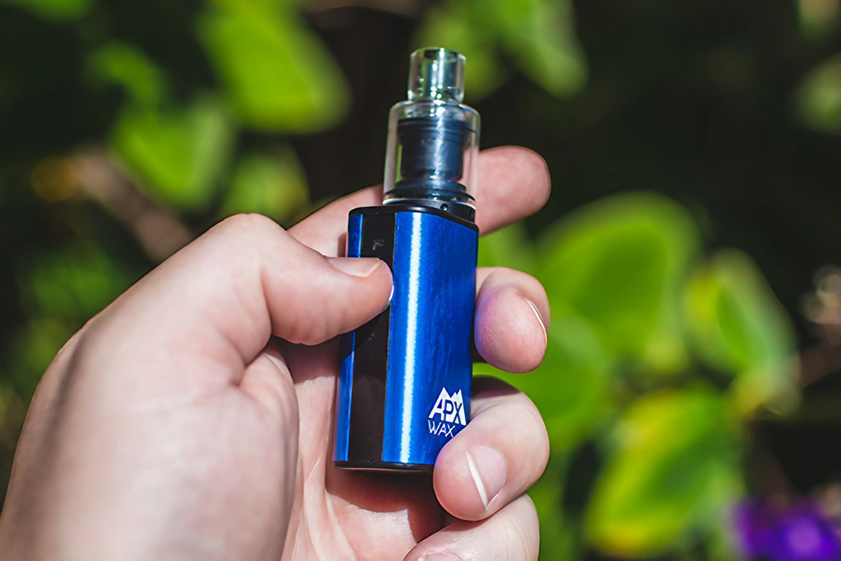 Hand holding Pulsar APX Wax Vaporizer in blue, compact design with quartz chamber, outdoor background