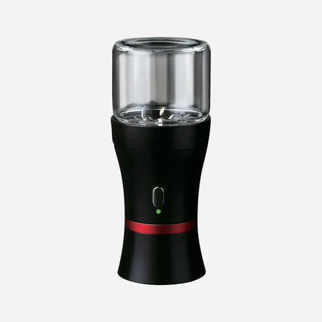 A sleek electric herb grinder with a black curved body, a red accent ring, and a clear glass chamber on top. A single button with a green light controls grinding, while sharp internal blades ensure efficient herb processing.