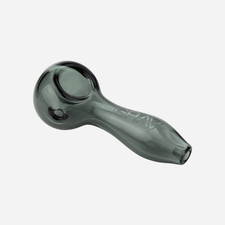 A glass handpipe with a smoky gray, semi-transparent finish. It has a classic spoon shape, featuring a rounded bowl on one end for packing material and a smooth, slightly curved stem that tapers toward the mouthpiece.