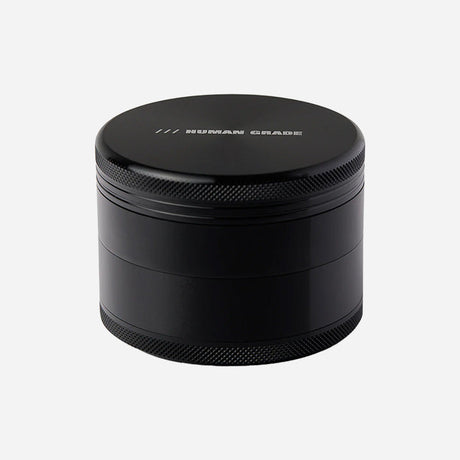 A black metal herb grinder with a sleek, matte finish. The lid features the engraved text "HUMAN GRADE" with three small slashes above it. The sides have textured grips for easy twisting, and it appears to be multi-chambered.