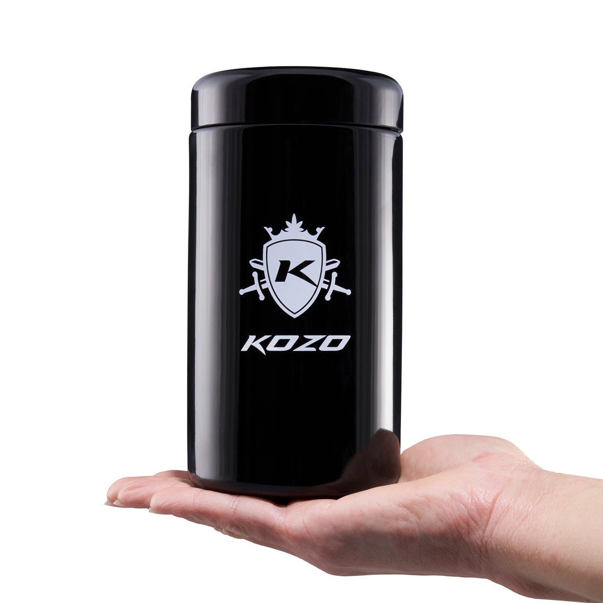 Kozo 1 oz black UV glass storage jar with the airtight lid on, held in one hand to show its size