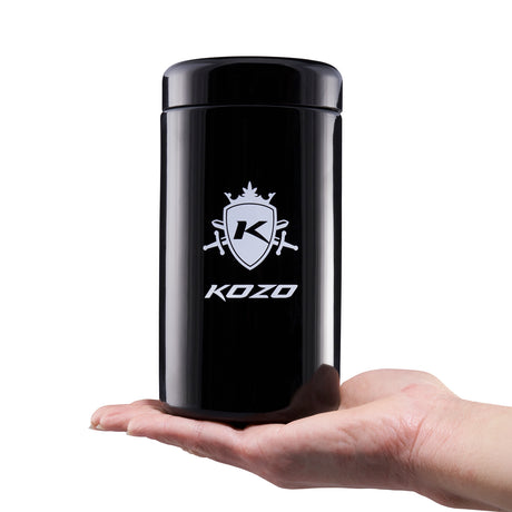 Kozo 1 oz black UV glass storage jar with the airtight lid on, held in one hand to show its size