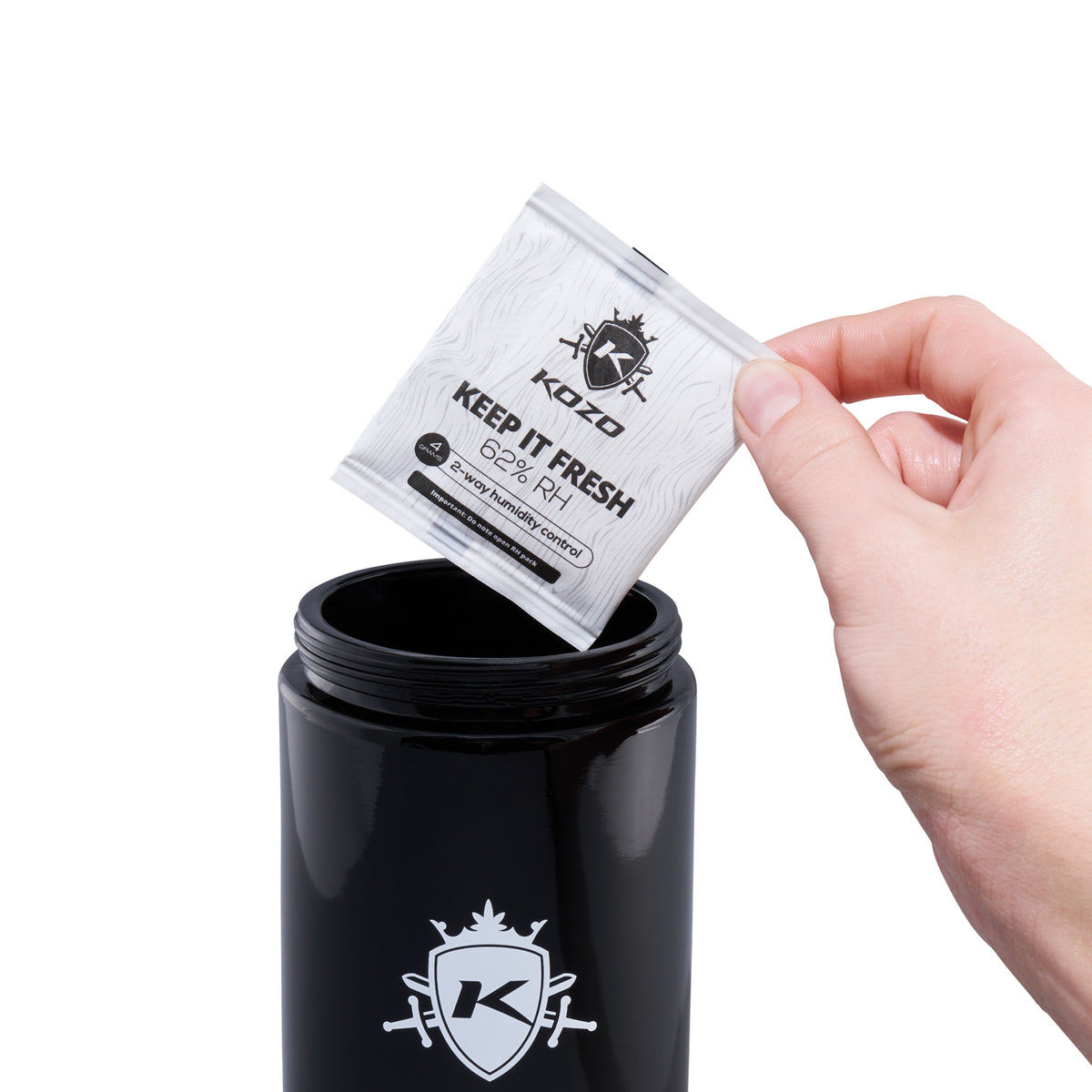 Kozo 1 oz black UV glass storage jar with a hand holding the humidity packet beside the open jar