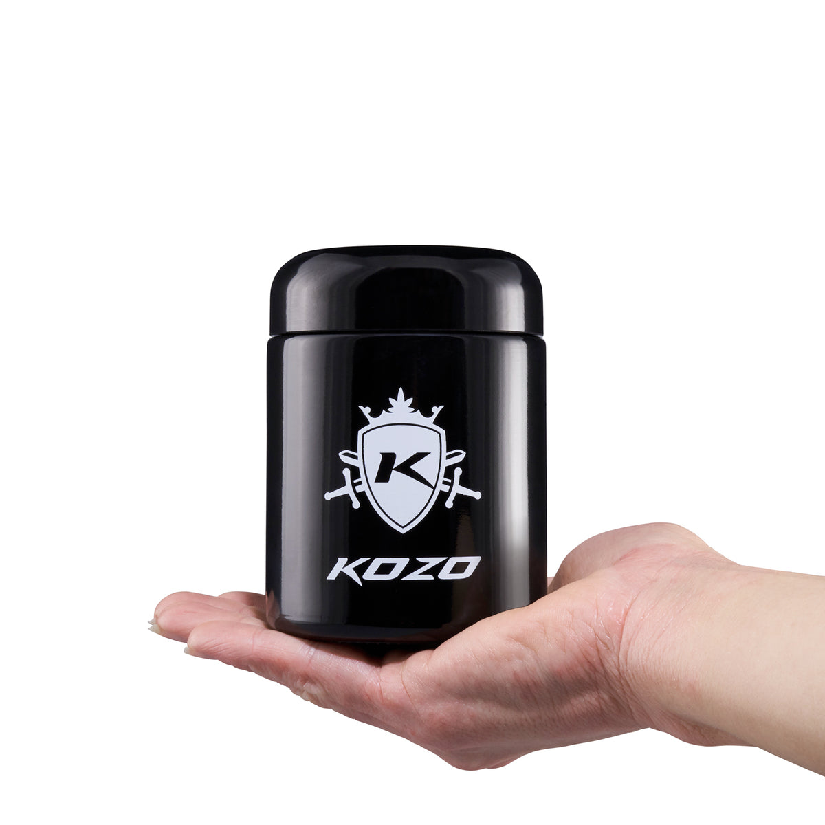 Kozo 1/2 oz black UV glass storage jar with airtight lid held in one hand to show its size