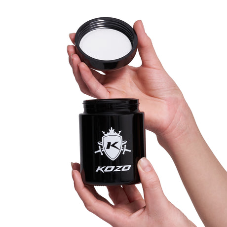 Kozo 1/2 oz black UV glass storage jar with a hand holding the airtight lid just above the jar