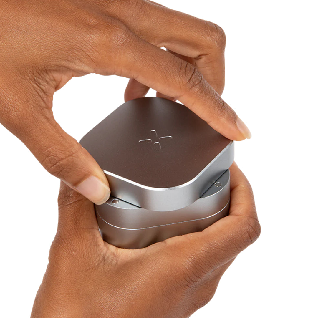 Close-up of hands holding a PAX Grinder in brushed metal, showcasing its compact design