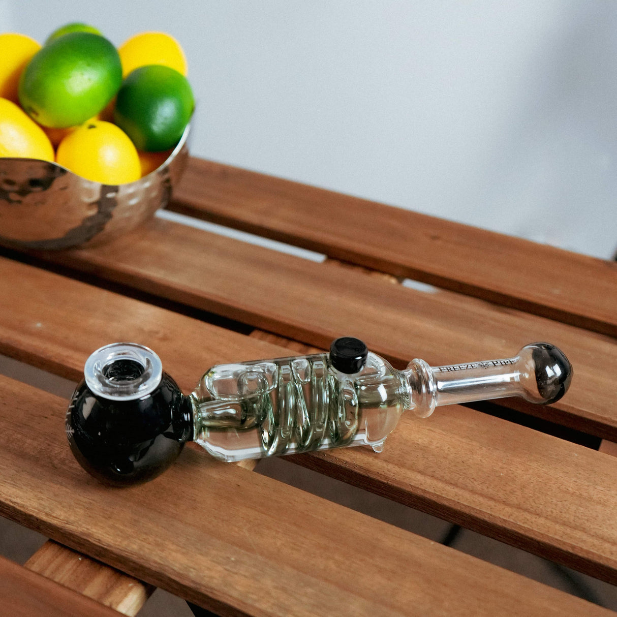 Freeze Pipe hand pipe in black and clear borosilicate glass, portable design, on wooden surface