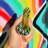 MAV Glass wigwag golden Professional Hand Pipe with Borosilicate Colored Glass, held against a graffiti wall