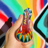 MAV Glass wigwag golden Professional Hand Pipe held in front of colorful graffiti