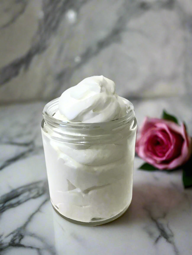 Elite Creed Natural Rose Body Butter in open jar, CBD-infused, on marble surface with pink rose