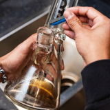 Close-up of hands using BoroBuddy™ Magnetic Cleaner on a glass bong, showing efficiency and ease of use.