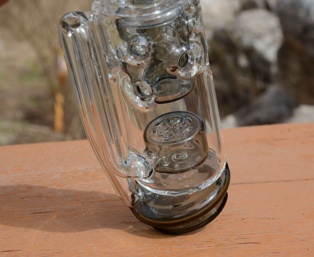Calibear Straight Fab Puffco Attachment in clear glass, angled side view on wooden surface