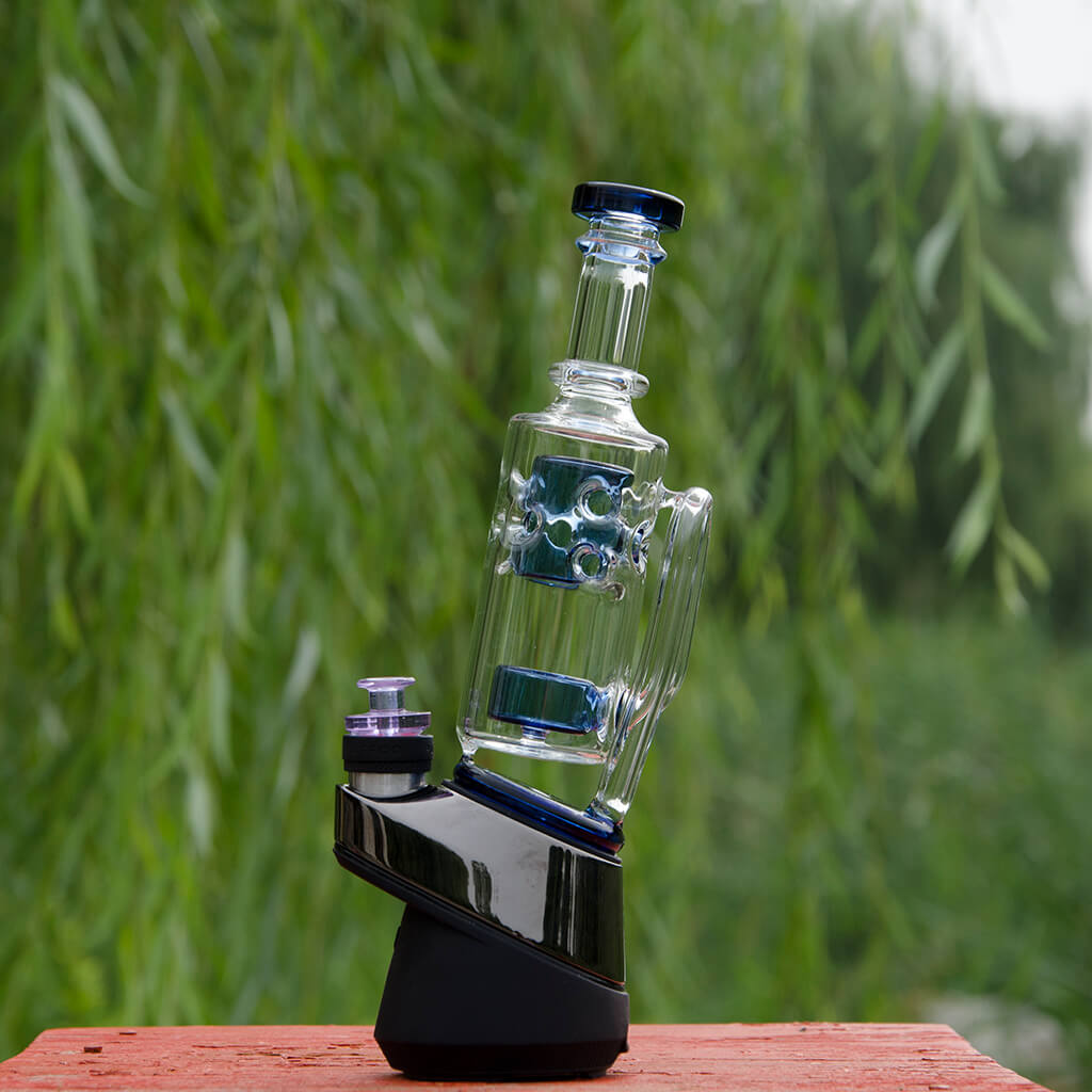 Calibear Straight Fab Puffco Attachment in clear glass with blue accents, side view on outdoor background