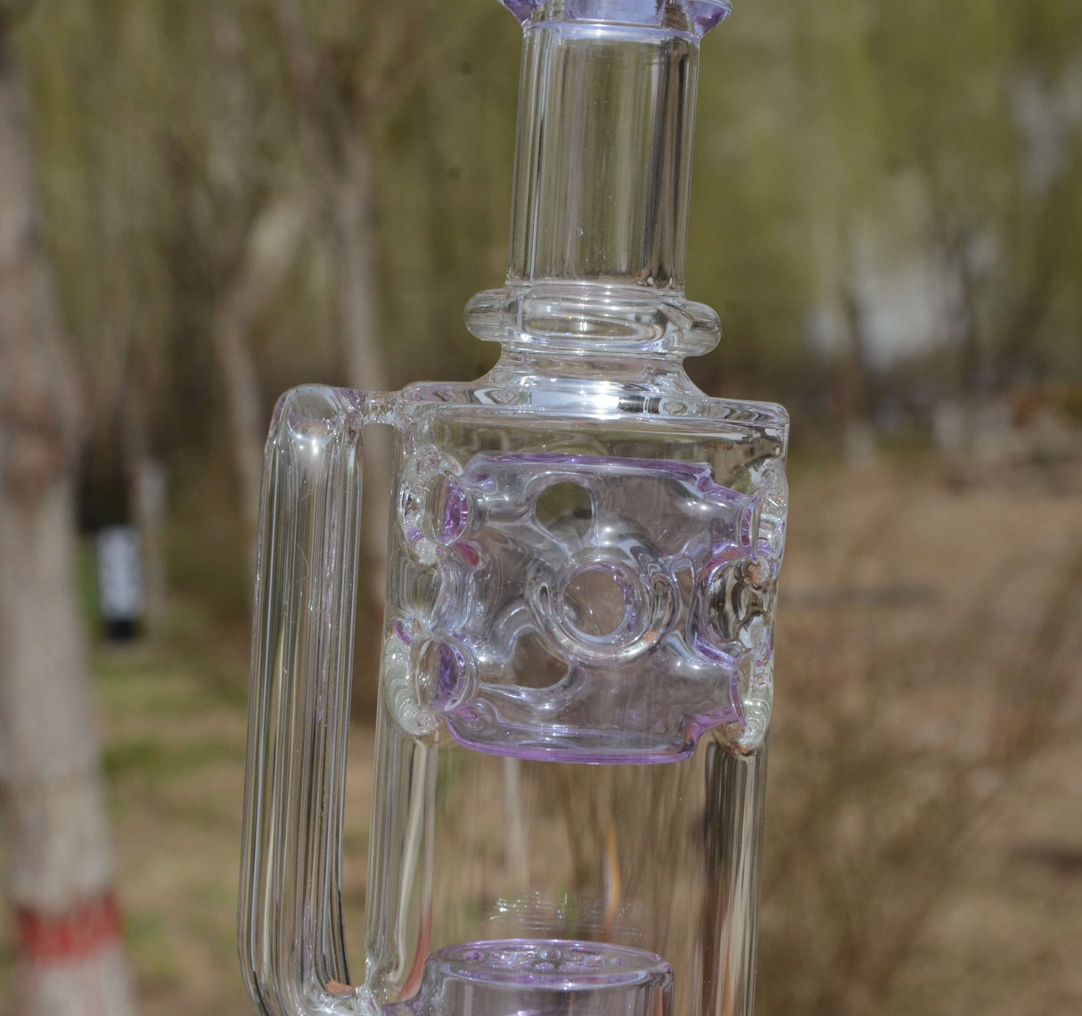 Calibear Straight Fab Puffco Attachment in clear glass with purple accents, outdoor background