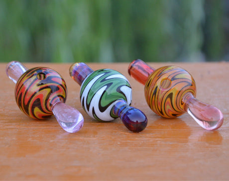 Calibear Wigwag Bubble Carb Caps in various colors with intricate glass patterns, side view on wooden surface