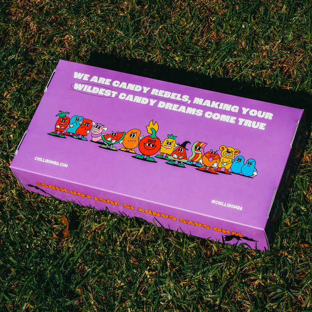 Chilli Bomba's Spooky & Spicy Mystery Box lying on grass, vibrant design with cartoon characters