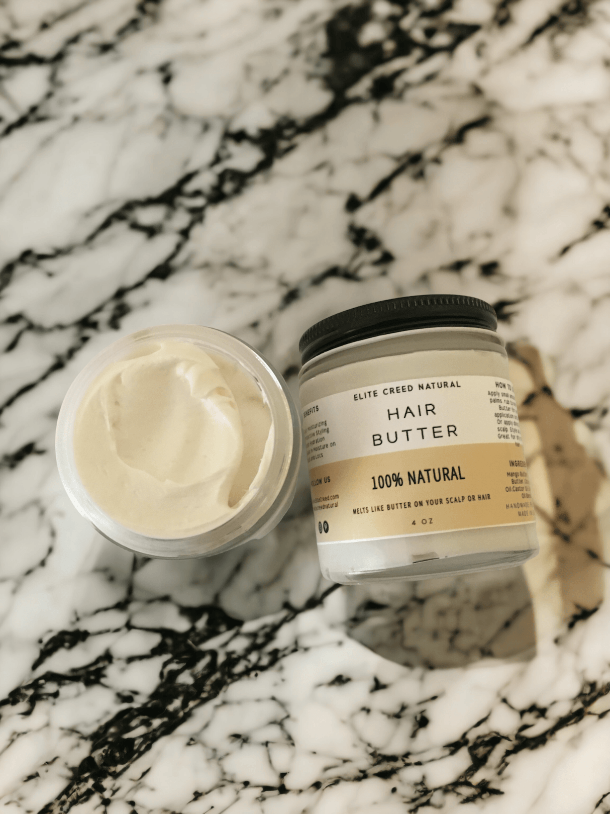 Elite Creed Natural Hair Butter with CBD, open jar on marble surface showing creamy texture