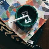 Hemper Asher "Cannaflage" green silicone ashtray with joint, angled view on patterned surface