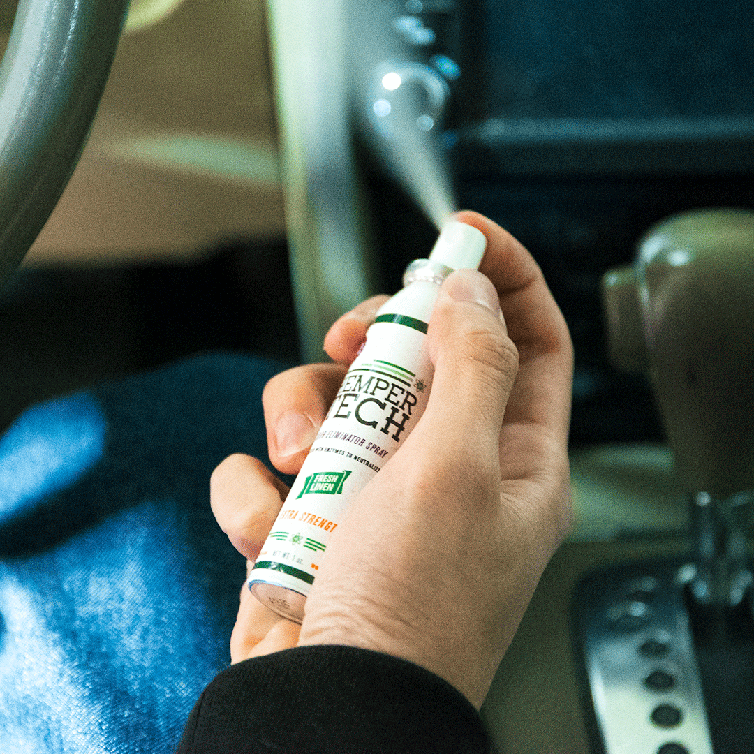 Hand holding Hemper Tech Odor Eliminator Spray in a car for smoke smell removal