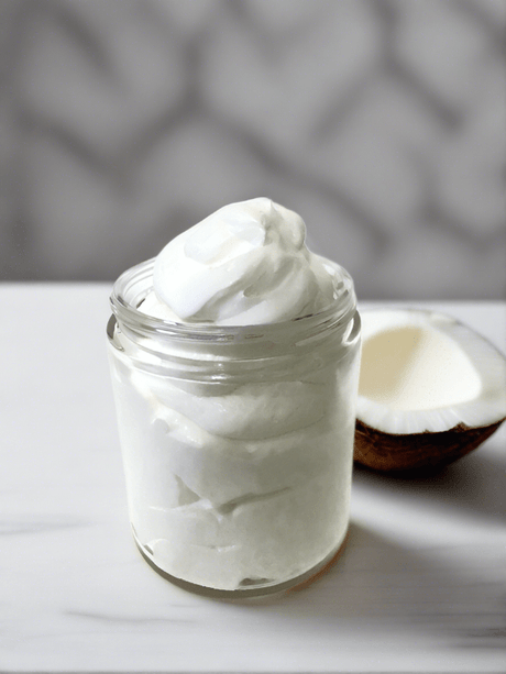 Elite Creed Natural Coconut Dream Body Butter in open jar with coconut half, front view on marble