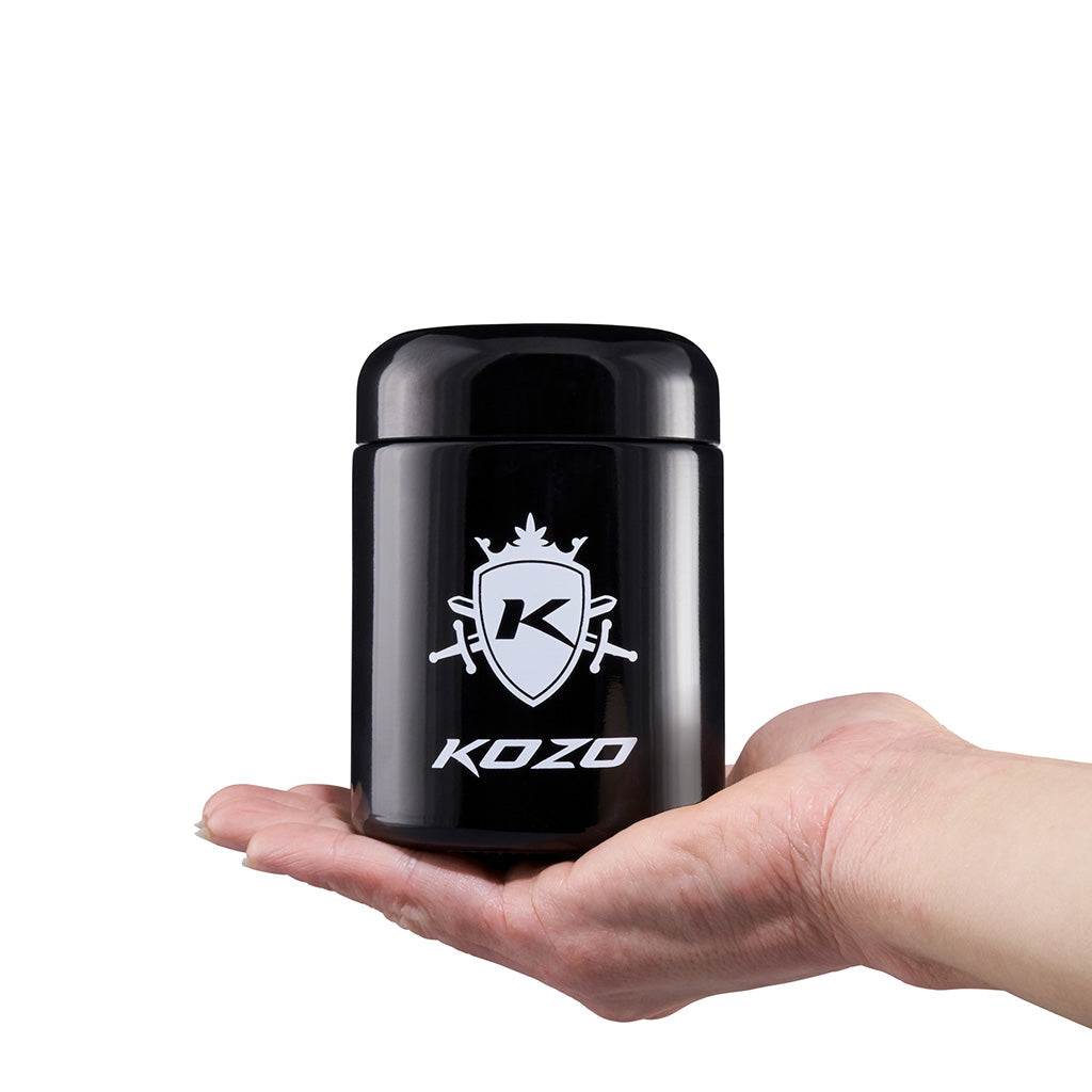 Kozo black UV glass storage jar held in one hand to show its size, with the airtight lid in place