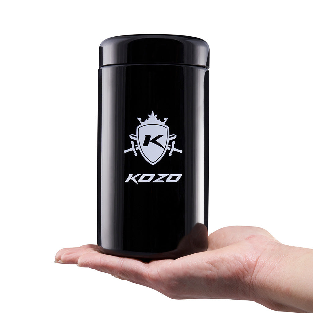Kozo black UV glass storage jar held in one hand beside the humidity packet that sits inside the jar