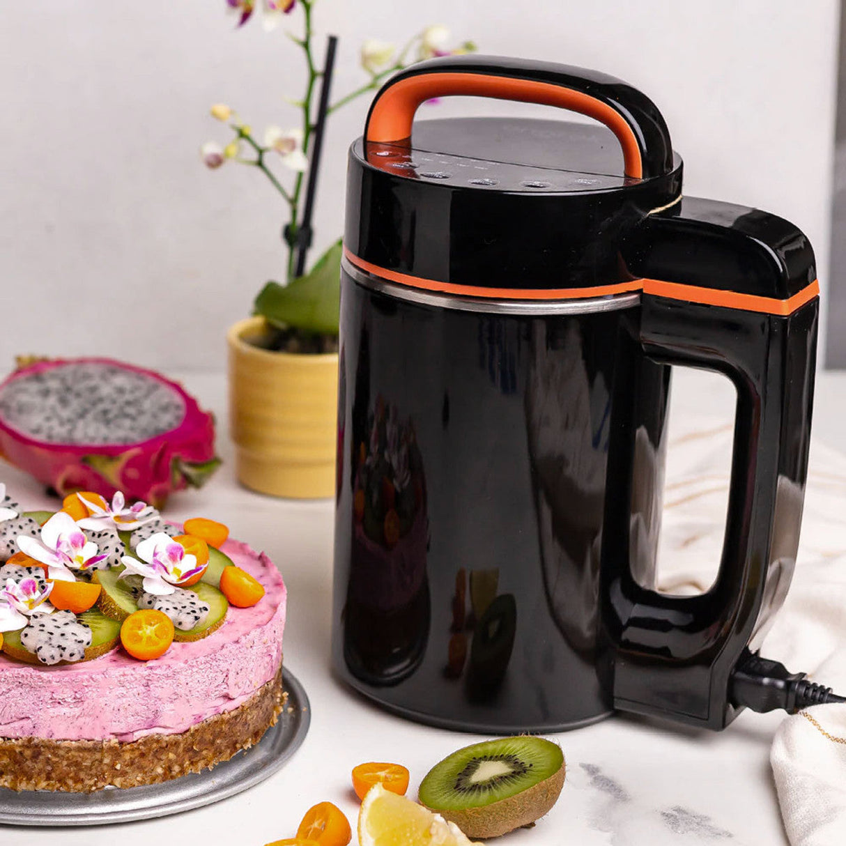 Ongrok Botanical Infuser Machine in black with orange trim, next to a fruit cake, front view