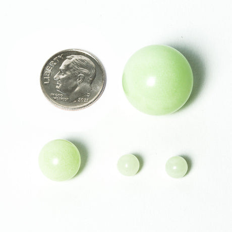 aLeaf Terp Pearls 4-Pack Mix glowing in the dark, next to a coin for scale, on a white background
