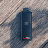 XVape Avant Dry Herb Vaporizer in black, portable design with ceramic chamber, on wooden surface
