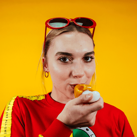 Person using Goody Bananza Hand Pipe by Goody Glass with vibrant yellow backdrop