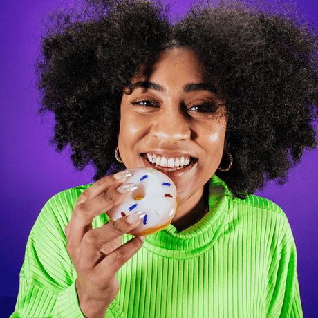 Goody Glass Donut Hand Pipe with a smiling person holding it, vibrant purple background