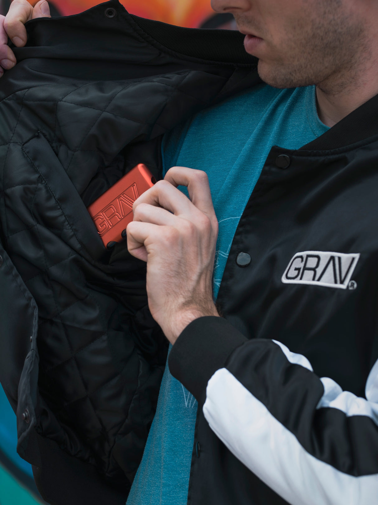 Close-up of a person wearing a GRAV Satin Bomber Jacket with logo and placing a wallet in the inner pocket