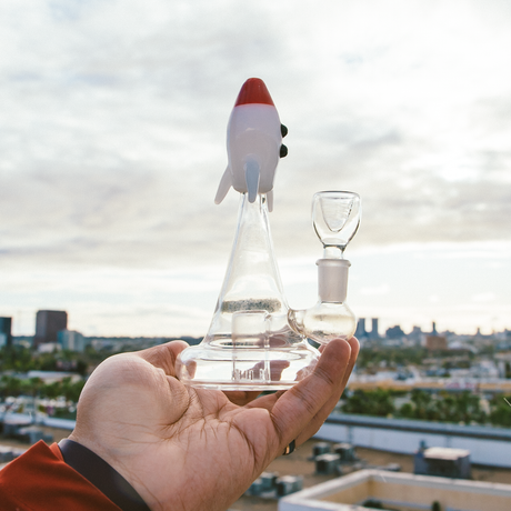 Hemper Blastoff Rocket Bong held in hand, clear glass with 14mm female joint, cityscape background