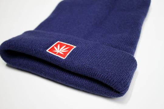 StonerDays blue beanie with red cannabis leaf logo, close-up angled view on white background